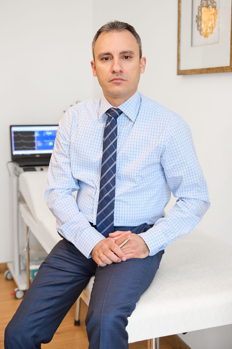 Ο νευρολόγος ποζάρει σοβαρά στον ιατρικό του χώρο, με εξοπλισμό διάγνωσης στο φόντο.