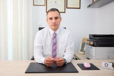 Ο νευρολόγος Βελίτσος Ιωάννης κάθεται σοβαρός στο γραφείο του, φορώντας άσπρο πουκάμισο και πολύχρωμη γραβάτα.